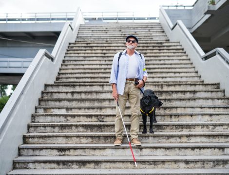 Senior blind man with guide dog walking down the stairs in city